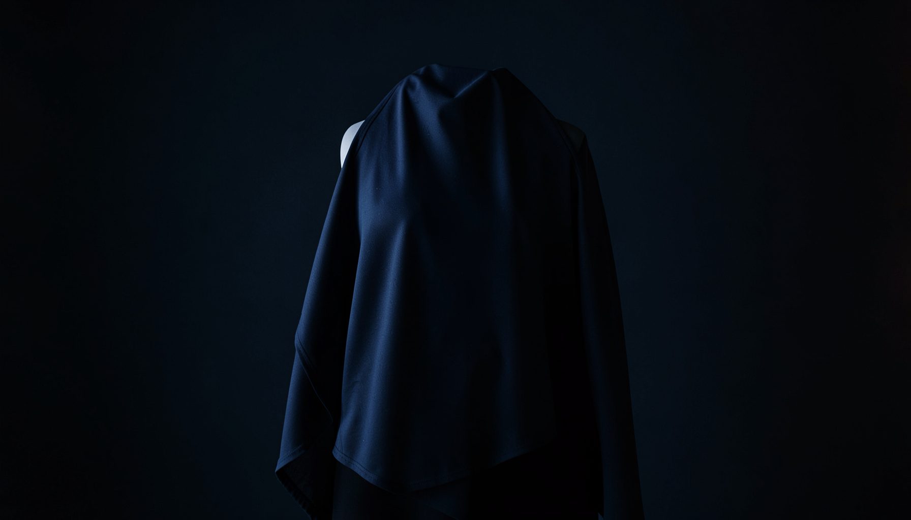 Dark atmospheric studio shot of body-shaping apparel draped on a minimalist form, deep navy shadows with soft warm highlights
