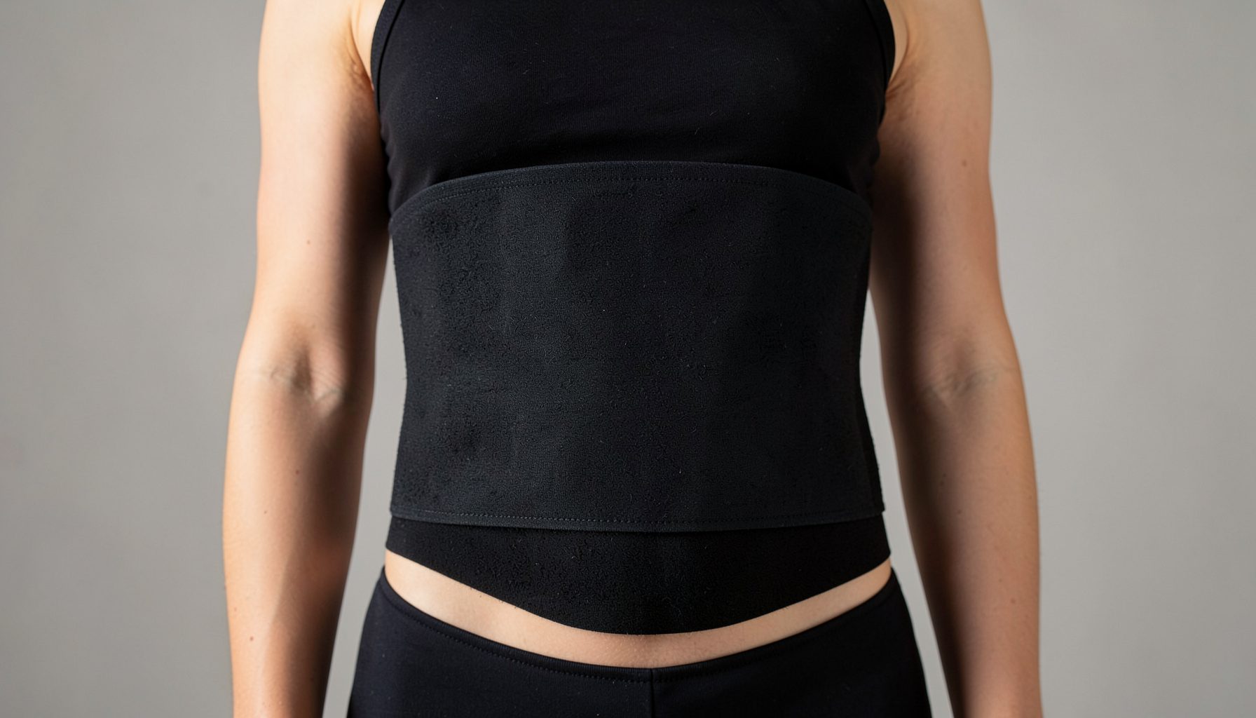 Close-up of a woman's midsection wearing a black waist trainer against a neutral studio background