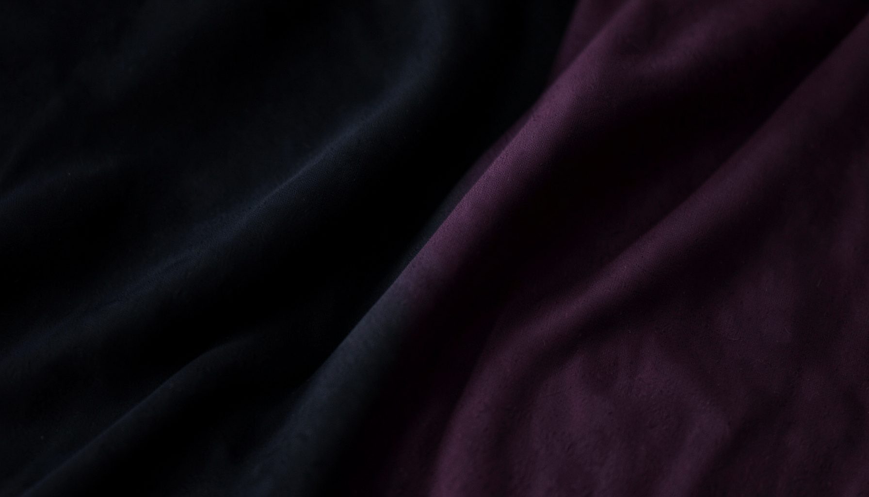 Dark atmospheric background with soft fabric folds in deep charcoal and muted plum tones, suggesting body-shaping apparel