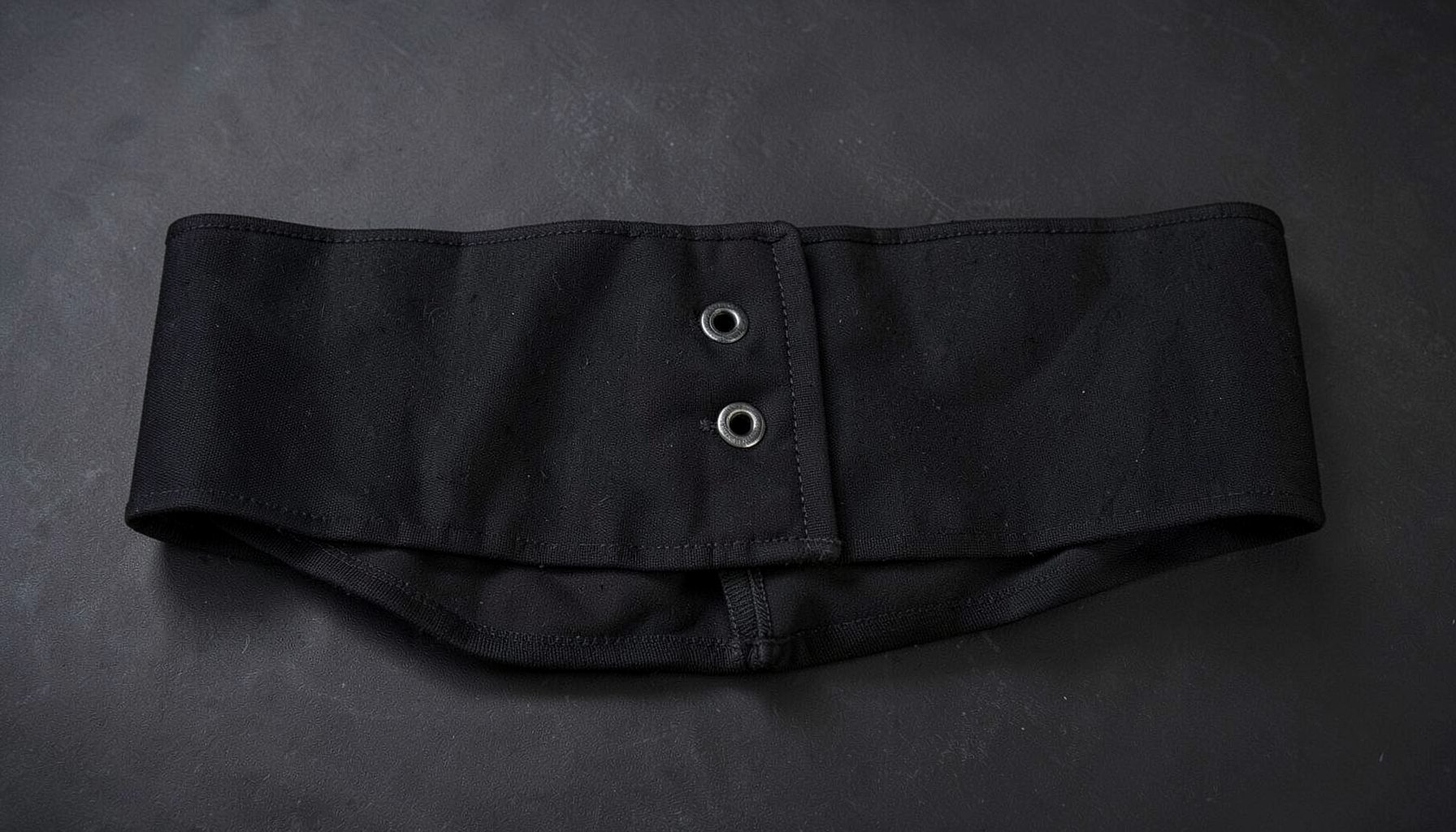 Black men's waist trainer band with hook-and-eye closure lying flat on a dark surface